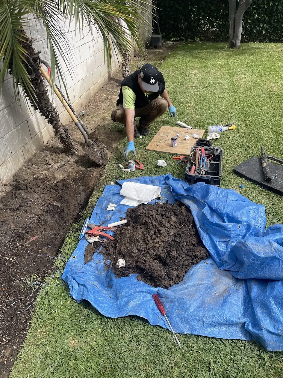 Technician trenching along a side yard to reach a deep underground sprinkler pipe break in Canoga Park