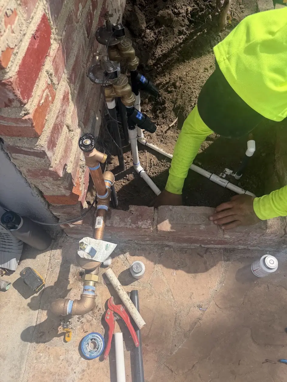 Technician rebuilding sprinkler valves beside a brick wall