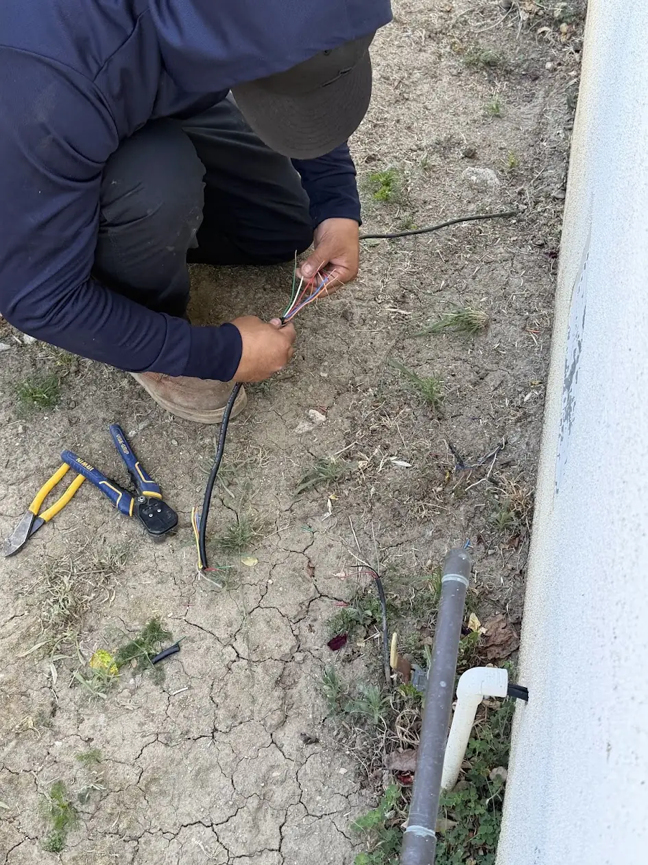 Technician splicing a damaged sprinkler control wire along the side of a house
