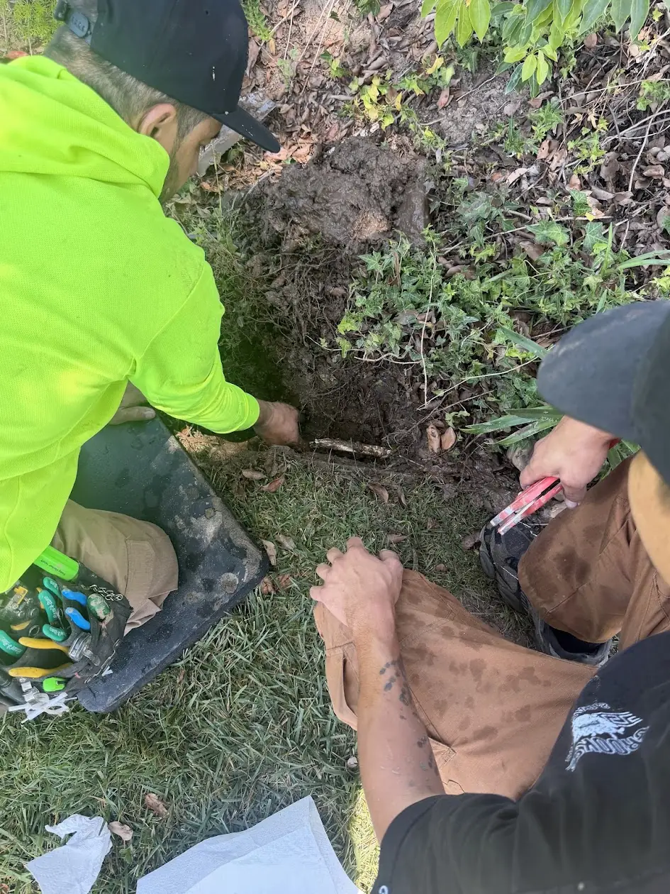 Two technicians digging to repair a broken underground sprinkler pipe