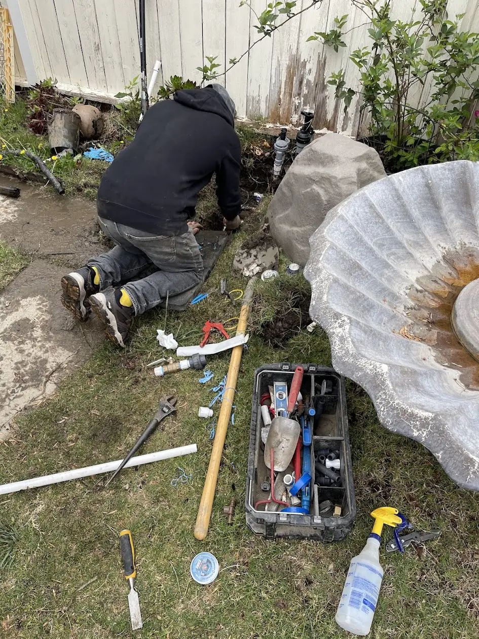Technician repairing a leaking sprinkler valve manifold in a Woodland Hills backyard