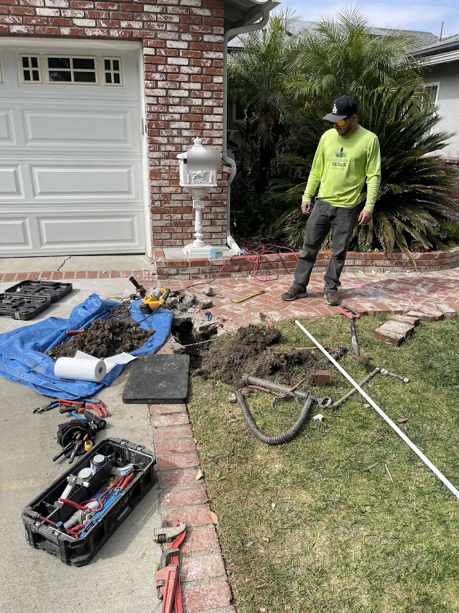 Valley Sprinkler Repair technician repairing a sprinkler pipe break under a brick walkway in Woodland Hills